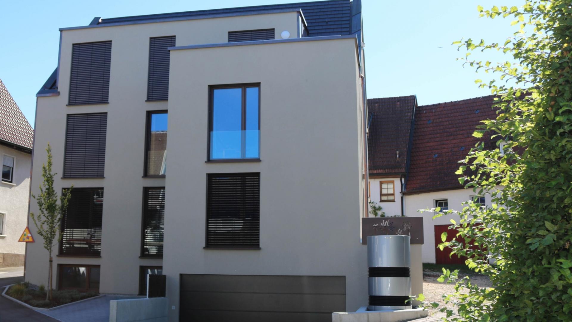 Ansicht eines modernen Mehrfamilienhauses in energieeffizienter Bauweise mit Wärmepumpe. Der geradlinig Baukörper wird durch große Fenster an der beigefarbenen Fassade strukturiert.